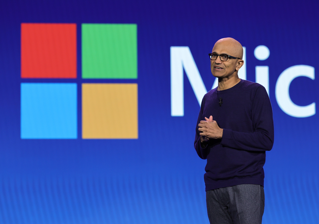 Satya Nadella in front of a background with the Microsoft logo